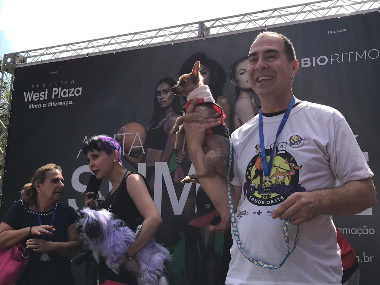 Momento de premiação do evento, com um dos donos levantando seu pet com uma das mãos 